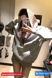 Person wearing a gray hoodie and plaid skirt taking a mirror selfie in a store.