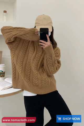 Person wearing a brown cable knit sweater and beige cap taking a mirror selfie.