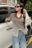 Woman standing next to a car holding a drink, wearing sunglasses and a ribbed sweater.