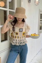 Woman wearing a crochet top and holding a bowl of lemons in a white-walled room.