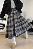 Person wearing a black coat, white shirt, plaid skirt, and white shoes in an indoor setting.
