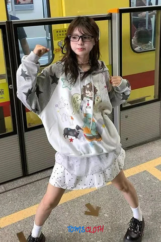 Person wearing a hoodie with cartoon designs in a subway setting, with 'TOMS CLOTH' branding.