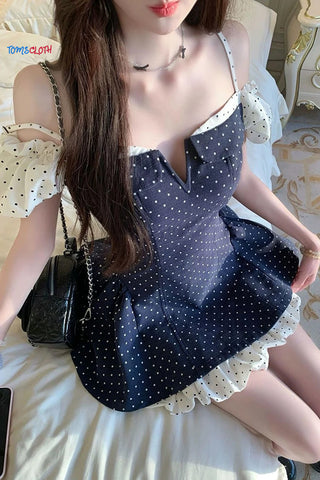 Woman wearing a navy blue dress with white polka dots and lace trim, sitting on a bed.