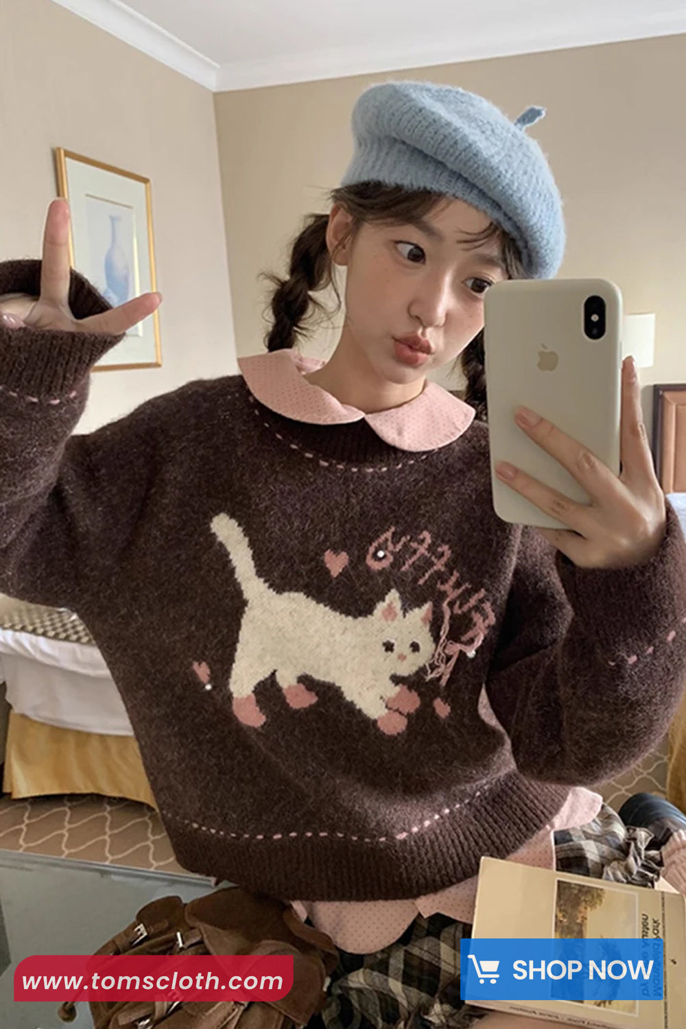 Person wearing a brown sweater with a cat design, taking a mirror selfie.