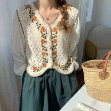 Person wearing a white blouse with a floral embroidered vest, standing next to a woven basket.