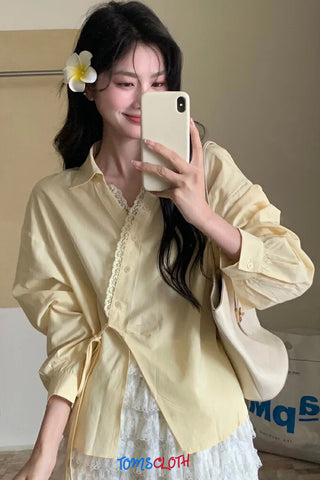 Woman in a yellow shirt taking a selfie with a phone, wearing a flower in her hair.