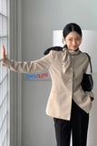 Woman wearing a beige blouse with a brand logo, standing indoors.