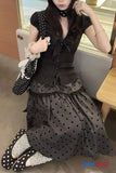 Person wearing a black polka dot dress with a bow tie and holding a polka dot shoe.