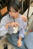 Person sitting at a table, drinking from a cup with a straw, wearing a striped shirt and jeans.