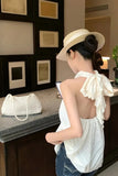 Woman in a white top with bow detail and straw hat in a room with framed pictures on the wall.
