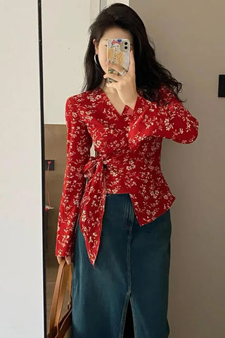 Person wearing a red floral blouse and blue jeans taking a mirror selfie.