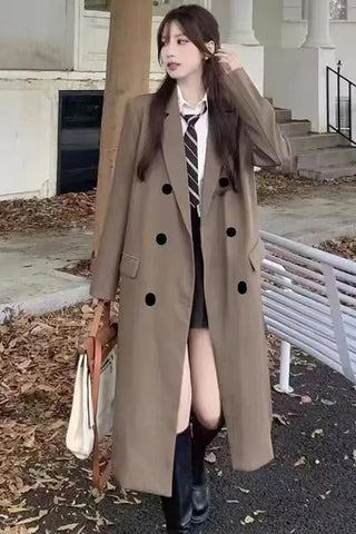Woman wearing a long brown coat with black buttons outdoors.