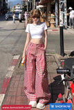 Woman in white crop top and red checkered pants standing on a street corner with a scooter nearby.