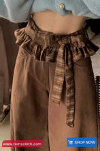 Brown pants with a plaid belt worn by a person, with a brand logo at the bottom.