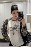 Person taking a mirror selfie wearing a camouflage jacket and graphic t-shirt.