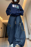 Person wearing a navy hoodie with colorful patches and blue jeans indoors.