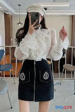 Person wearing a white blouse with sheer sleeves and a black skirt with embroidery in an indoor setting.