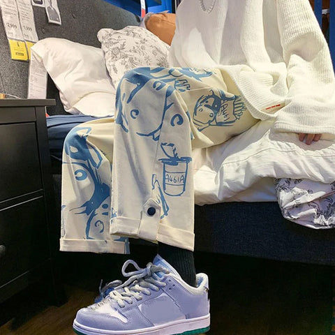 Person wearing a white jacket with blue patterns, sitting on a bed with a white blanket.