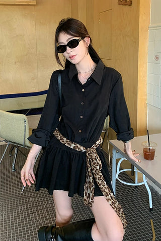 Woman in a black dress with a leopard print belt sitting in a cafe.