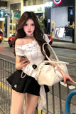 Woman in a white off-shoulder top and black skirt holding a beige handbag on a city street.
