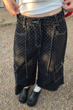 Person wearing black pants with white polka dots and a white top outdoors.