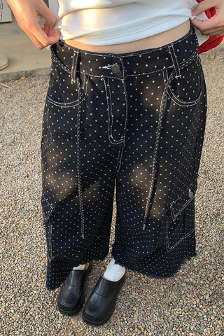 Person wearing black pants with white polka dots and a white top outdoors.