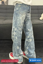 Light blue jeans with floral patterns worn by a person, sitting on a gray couch.