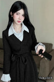 Woman in a black coat holding a phone indoors