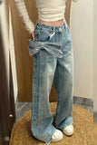 Person wearing blue jeans with a large bow detail, standing on a wooden stool.