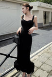Woman in a black dress with ruffled bottom standing on a sidewalk.