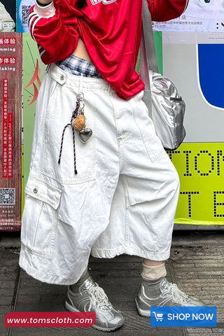 Person wearing a red jacket, white pants, and gray shoes with a silver bag.
