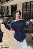 Woman wearing a blue off-shoulder top and white pants in an outdoor setting.