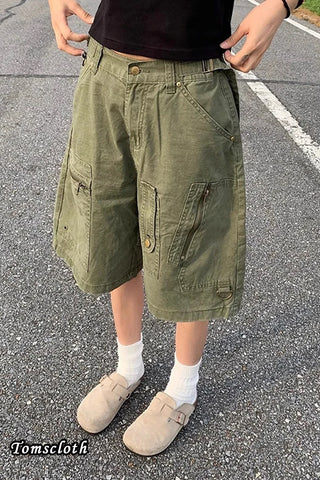 Person wearing olive green shorts on a road with 'Tomscloth' branding.