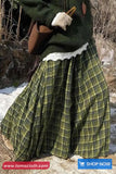 Person wearing a green plaid skirt with a white lace top, holding a brown bag outdoors.