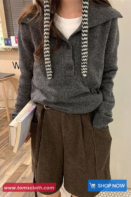 Person wearing a gray hoodie with drawstrings and brown shorts, holding a book indoors.