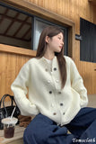 Woman wearing a white jacket with black buttons sitting outdoors.