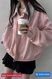 Person wearing a pink jacket holding a coffee cup against a plain background