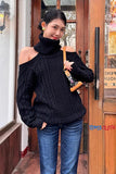 Woman wearing a black off-shoulder sweater and blue jeans standing in front of a store entrance.