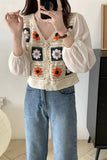 Person wearing a colorful crochet vest over a white blouse and blue jeans.