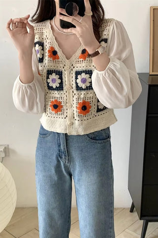 Person wearing a colorful crochet vest over a white blouse and blue jeans.
