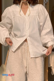Person wearing a white blouse with long sleeves and beige pants indoors.