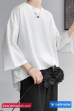 Person wearing a white blouse with bell sleeves and black pants on a gray background
