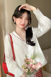 Woman in a white blouse holding a bouquet of flowers and a red bag.