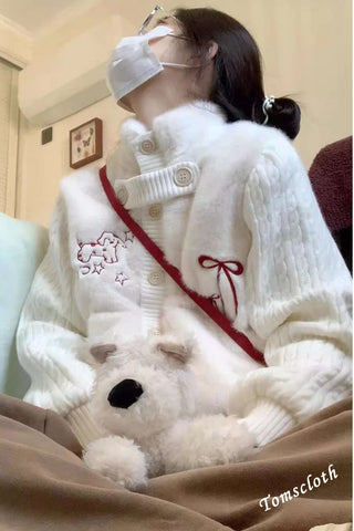 Person wearing a white sweater with a red bow and holding a white teddy bear, sitting on a couch.