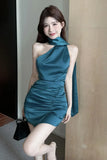 Woman in a teal dress standing indoors against a neutral wall.