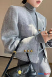 Person wearing a gray blazer with gold buttons and holding a black handbag.