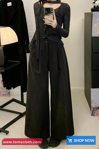 Person wearing a dark gray outfit with wide-leg pants in a minimal indoor setting.