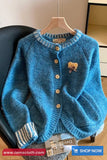 Blue knitted cardigan on a hanger with a visible brand tag, displayed indoors.