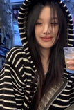 Person wearing a black and white striped hoodie holding a drink.