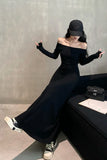 Person wearing a black off-shoulder dress and sneakers, sitting on a bench.